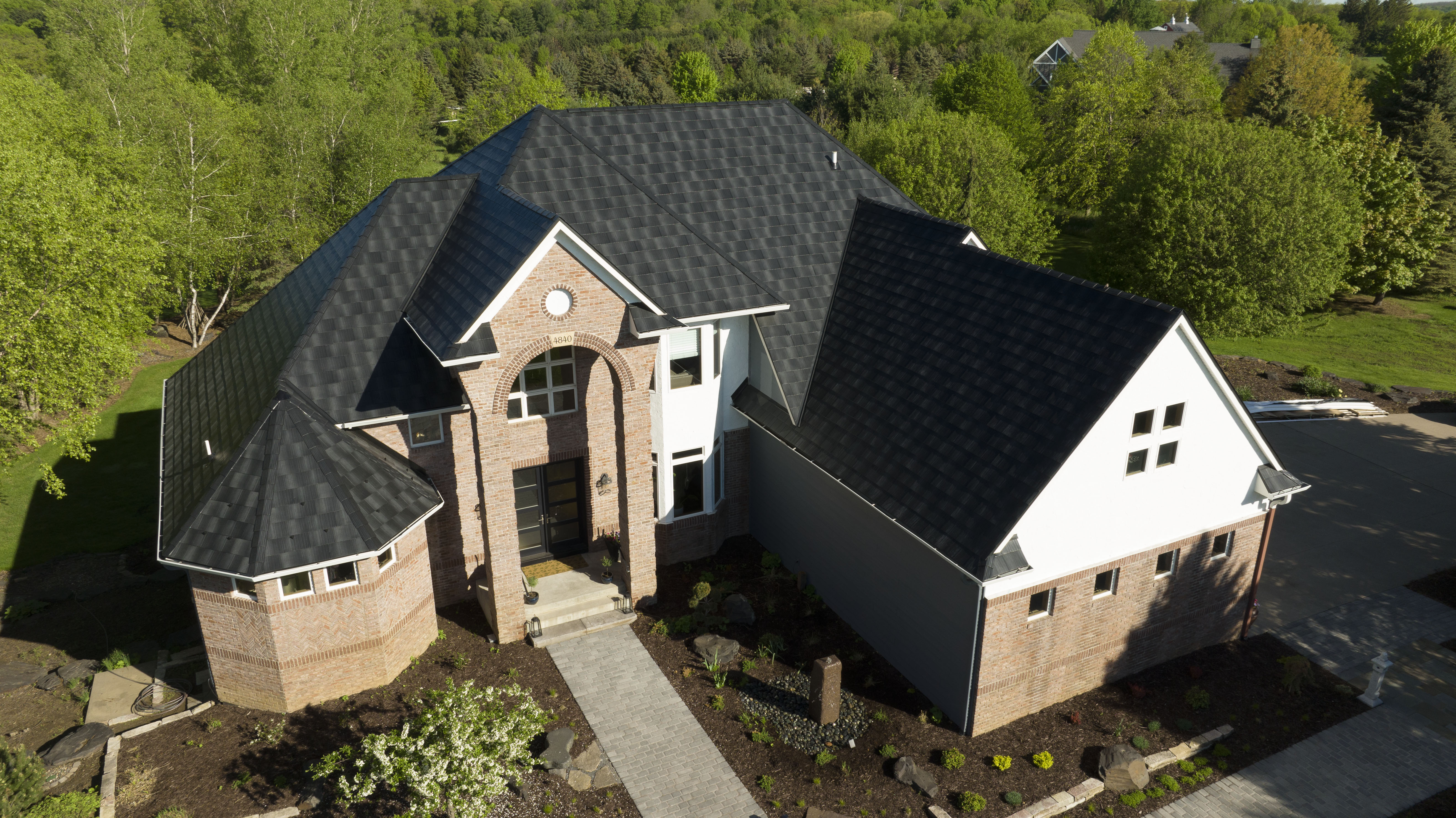 Dark textured roof on a brick home surrounded by trees